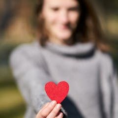 a blurred image of a young woman holding up a red heart to the camera