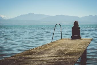 woman sitting on a jetty with a backdrop of mountains